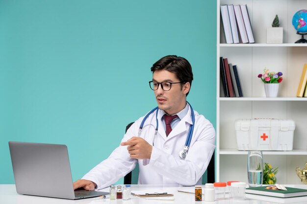 Médico joven médico inteligente en bata de laboratorio que trabaja de forma remota en la computadora