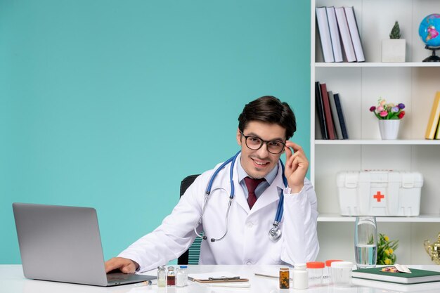 Médico joven médico inteligente en bata de laboratorio trabajando de forma remota en la computadora sonriendo