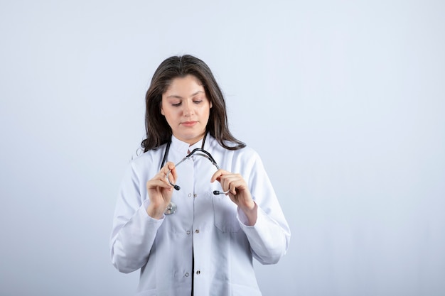 médico joven que mira el estetoscopio en la pared blanca.