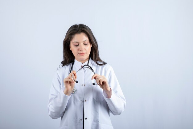 médico joven que mira el estetoscopio en la pared blanca.