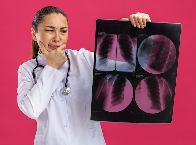 Foto gratuita médico joven sosteniendo una radiografía de los pulmones mirándolo con expresión confusa