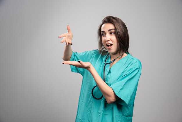 Médico joven en uniforme de pie sobre la pared gris.