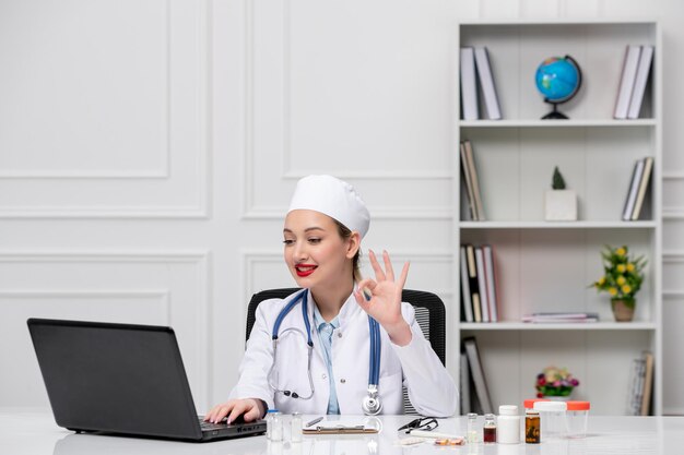Médico lindo y encantador doctor en bata de laboratorio blanca y sombrero con videollamada hablando por computadora al cliente