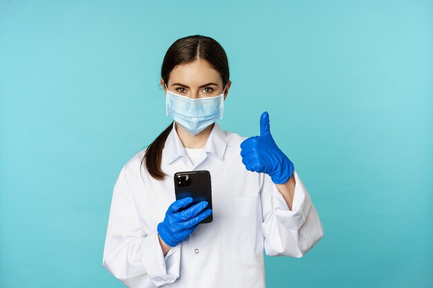 Médico en línea y clínica mujer joven con mascarilla médica usando un teléfono inteligente para el cliente remoto en línea...