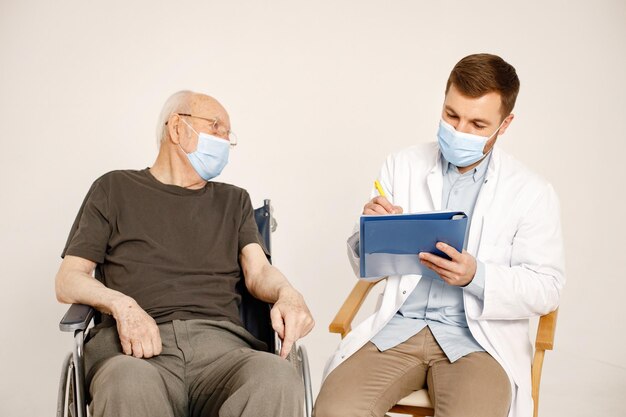 Médico masculino y anciano en silla de ruedas aislado en un fondo blanco