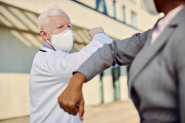 Médico masculino con mascarilla facial chocando con una mujer de negocios durante la epidemia de coronavirus