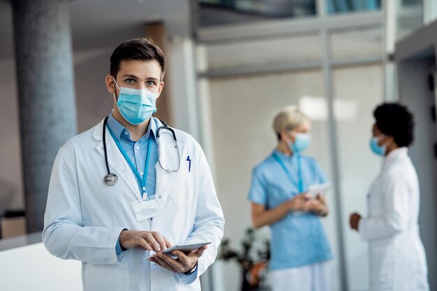 Médico masculino con mascarilla trabajando en tableta digital en la clínica