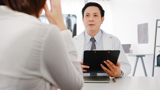 El médico masculino serio de Asia en uniforme médico blanco que usa el portapapeles está brindando excelentes noticias sobre los resultados