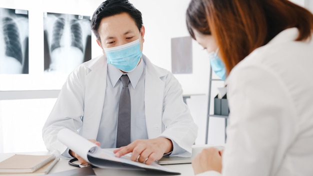 El médico masculino serio de Asia usa una máscara protectora que usa el portapapeles está brindando excelentes noticias sobre los resultados