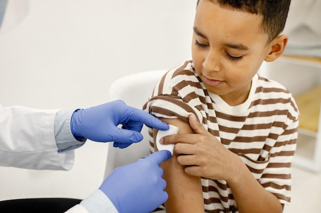 Médico masculino sosteniendo un algodón en los hombros de un niño después de una vacunación