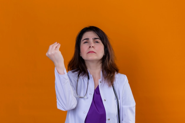 Médico de mediana edad con bata blanca y con estetoscopio gesticulando con la mano levantada haciendo gesto italiano sobre pared naranja aislada