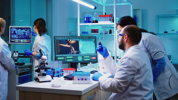 Médico microbiólogo tomando un tubo de muestra de sangre de rack con máquinas de análisis en el fondo del laboratorio