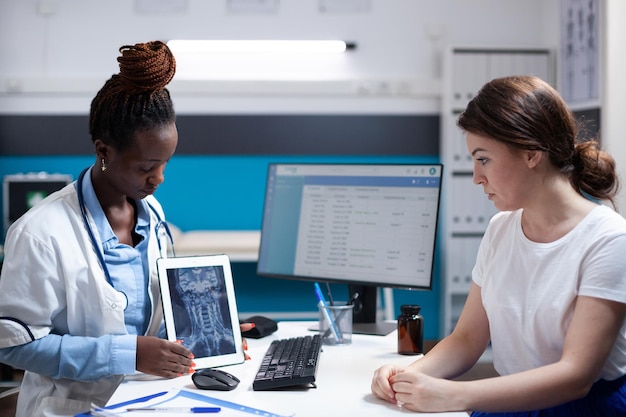 Foto gratuita médico mostrando lesión de vértebras cervicales dolor de cuello resultados de tomografía computarizada de rayos x en la tableta al paciente durante la cita médica. especialista en atención médica diagnosticando a la mujer después del chequeo de síntomas