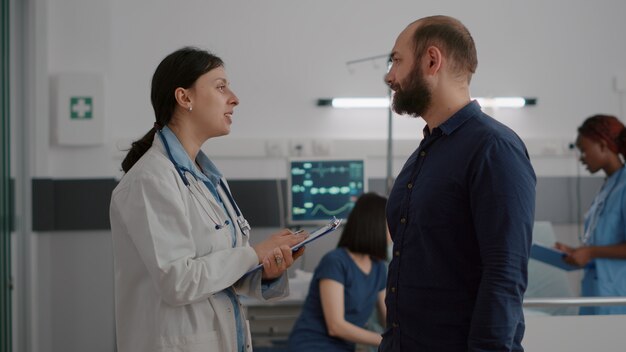 Médico de la mujer practicante discutiendo la experiencia médica con el padre preocupado durante el examen de recuperación