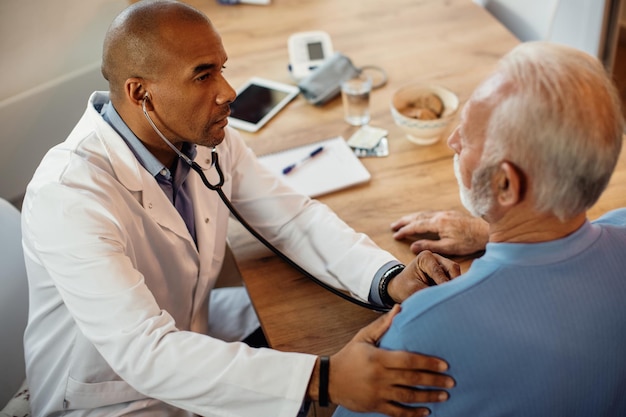 Médico negro que examina a un paciente mayor con un estetoscopio en un hogar de ancianos