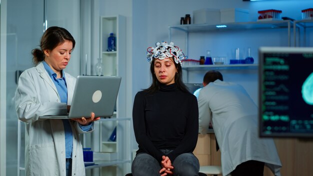 Médico neurólogo especialista tomando notas en la computadora portátil preguntando los síntomas del paciente ajustando auriculares eeg de alta tecnología