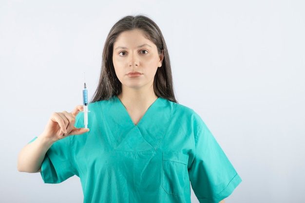 Médico o enfermera en uniforme verde sosteniendo una jeringa en blanco.