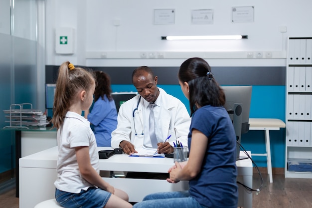 Médico pediatra afroamericano escribiendo experiencia en enfermedades en el portapapeles