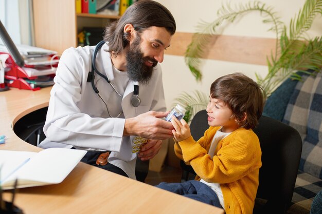 Médico pediatra examinando a un niño en el consultorio médico comfortabe. Concepto de salud, infancia, medicina, protección y prevención. El niño confía en el médico y siente emociones tranquilas y positivas.