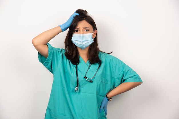 Foto gratuita médico perplejo en máscara médica y guantes pensando sobre fondo blanco. foto de alta calidad