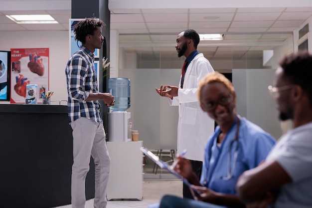 Médico y persona hablando en el vestíbulo de la sala de espera en el centro de salud para hacer una consulta médica y una visita de control. Tratamiento del diagnóstico de enfermedades con medicamentos y tratamiento, examen en la sala de espera.