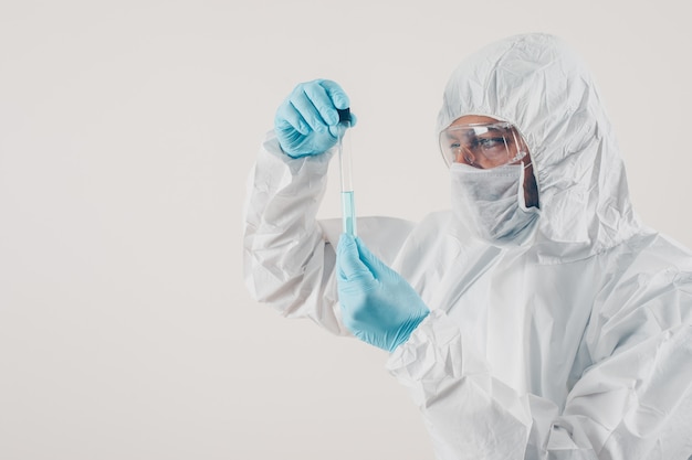 Un médico de pie y sosteniendo la medicina en fondo claro en guantes médicos y traje de protección.