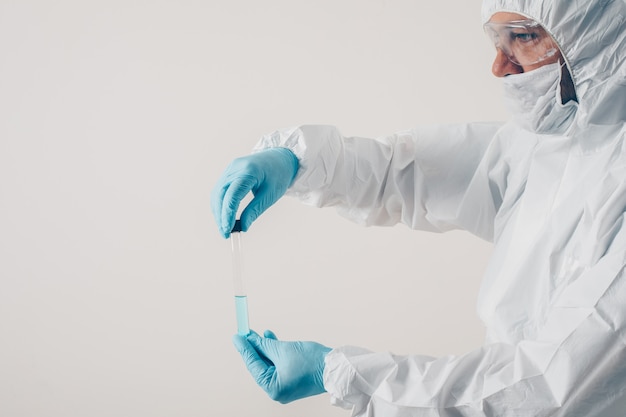 Un médico de pie y sosteniendo la medicina en fondo claro en guantes médicos y traje de protección.