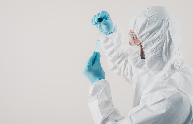 Un médico de pie y sosteniendo la medicina en guantes médicos y traje protector en fondo claro.