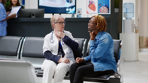 Médico principal que consulta a un paciente afroamericano en la recepción del hospital, hablando sobre el tratamiento de la salud y el diagnóstico de la enfermedad. doctor y mujer sentada en el vestíbulo de la sala de espera.