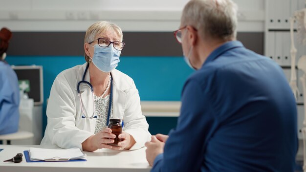 Médico principal que da un frasco de pastillas como medicamento recetado a un paciente enfermo en el examen durante una pandemia. Tratamiento con vitaminas, analgésicos, fármacos y medicamentos en matraz para curar enfermedades.