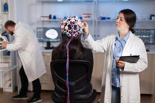 Médico profesional en neurociencia que desarrolla tratamiento para enfermedades neurológicas examinando la evolución del paciente. Investigador médico ajustando auriculares EEG analizando las funciones cerebrales y el estado de salud.