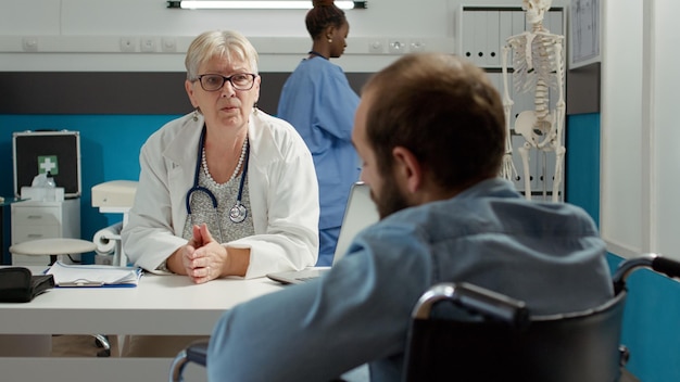 Médico que consulta a un usuario de silla de ruedas en una oficina apta para discapacitados para curar una condición de salud crónica. Hombre con discapacidad física que asiste a una cita de control, recibe asesoramiento y apoyo.