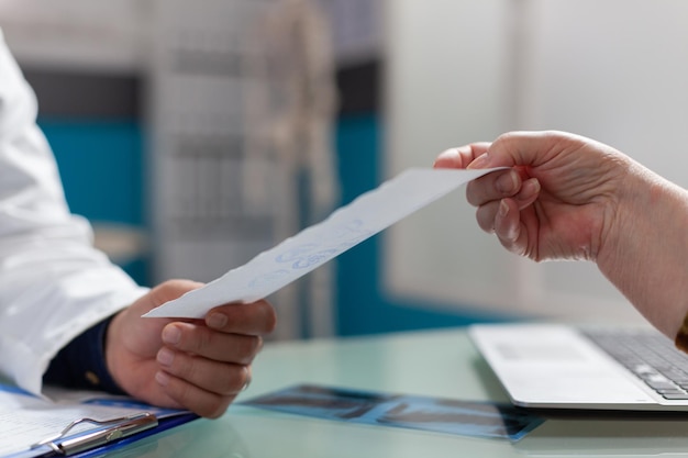 Médico que entrega el documento de prescripción al paciente en el gabinete, después de una consulta médica. Médico que tiene un informe de chequeo para dar tratamiento a una persona jubilada en la oficina de atención médica. De cerca