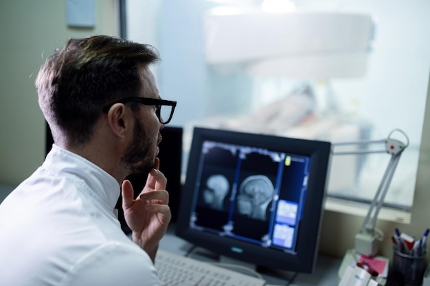 Médico que examina los resultados de la resonancia magnética de un paciente en el monitor de la computadora en el hospital