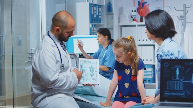 Médico que muestra gráficos de esqueleto en tableta durante la consulta. Médico especialista en medicina que brinda servicios de atención médica examen de tratamiento radiográfico en el hospital