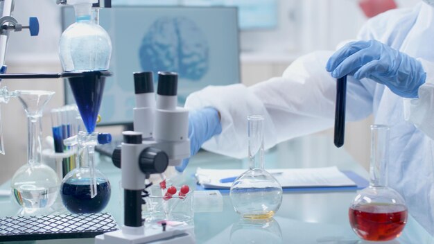 Médico químico investigador científico que trabaja con cristalería transparente que mezcla una solución líquida durante el experimento de microbiología en el laboratorio del hospital. Equipo médico en mesa. Concepto de medicina