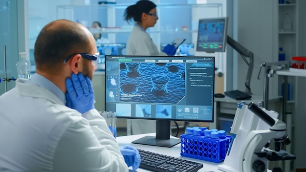 Médico químico preocupado trabajando en pc examinando la evolución de la vacuna en un laboratorio científico moderno equipado