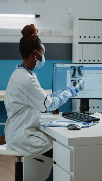 Médico con radiografía para examen con el paciente durante la pandemia de coronavirus. Médico explicando los resultados del escaneo de rayos X y el diagnóstico a la mujer, usando máscaras faciales para su protección.