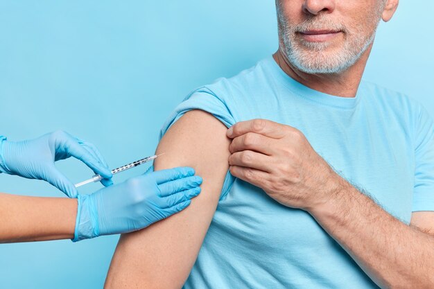 Un médico sin rostro inyecta la vacuna covid 19 a un paciente anciano que usa guantes protectores de goma.