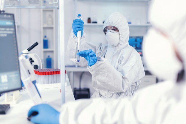 Médico de la salud que toma la muestra del tubo de ensayo con micropipeta. Equipo de microbiólogos en el laboratorio de investigación realizando un experimento durante la pandemia global con covid19.