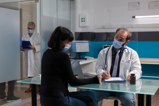 Médico de salud tomando notas en la consulta de chequeo en el gabinete, haciendo un examen con el paciente para curar la enfermedad. Médico escribiendo diagnóstico y tratamiento en papel durante la pandemia de covid 19.