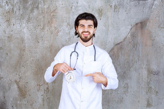 Médico de sexo masculino con un estetoscopio sosteniendo un reloj despertador.