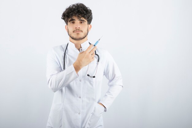 Médico de sexo masculino en uniforme blanco con estetoscopio con jeringa.