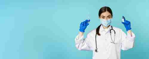 Foto gratuita médico sonriente del personal médico con mascarilla y guantes de goma que muestran jeringa y vacuna de covid p