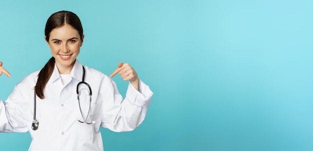 Médico sonriente trabajador médico señalando con el dedo el cartel de la clínica del logotipo que muestra un anuncio con w