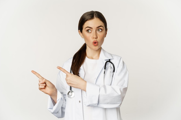 Médico sorprendido señalando con el dedo a la izquierda y mirando el banner del logotipo que muestra la publicidad de la clínica...