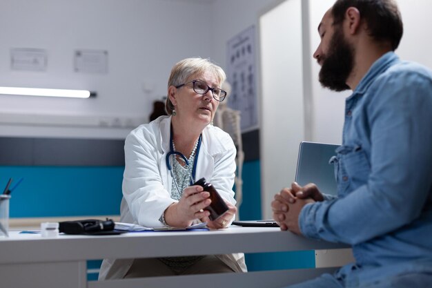 Médico sosteniendo una botella de píldoras para dárselas al paciente enfermo en la visita de control. Médico general que da un frasco con medicamentos recetados y tratamiento para la atención médica y el apoyo al hombre.