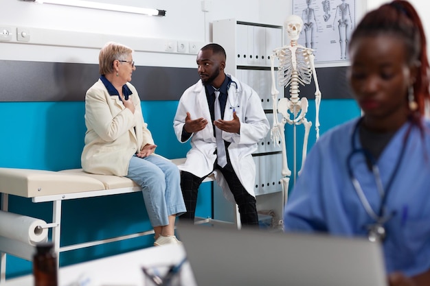 Médico terapeuta afroamericano explicando el diagnóstico de enfermedad al paciente jubilado senior discutiendo el tratamiento con medicamentos durante el examen médico en la oficina del hospital. Servicios de salud