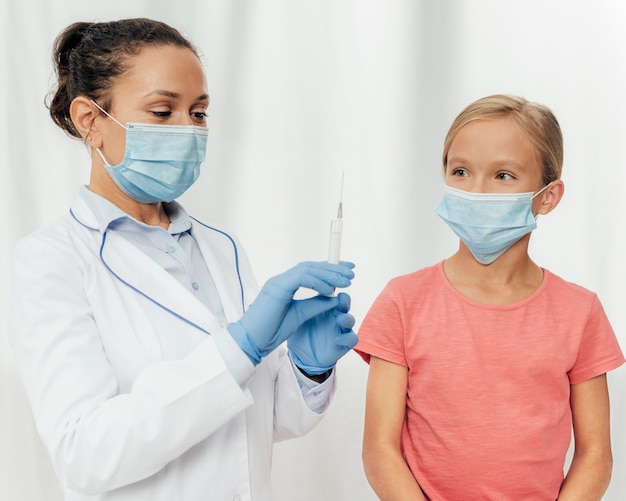 Médico de tiro medio y niña con máscaras