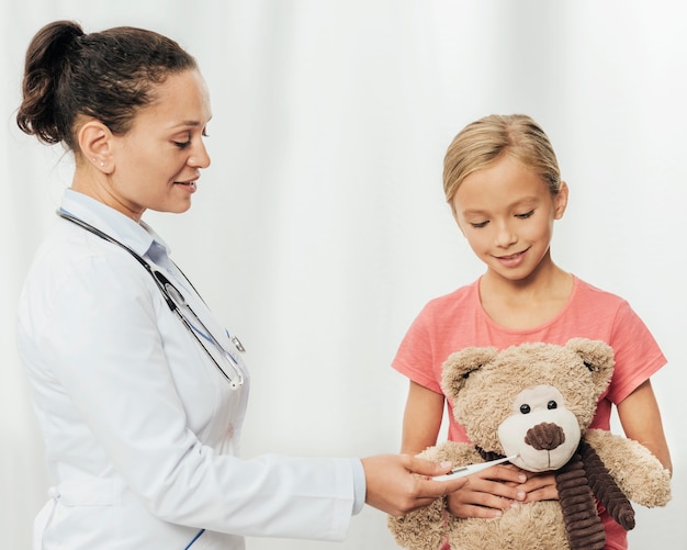 Médico de tiro medio y niña con oso